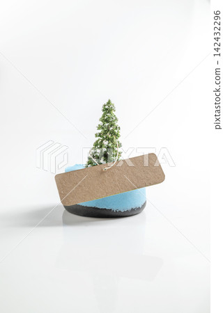 Miniature snow-dusted pine tree on a blue base with a blank craft paper label, isolated on a white background. Mockup or Copyspace Miniature snow-dusted pine tree on a blue base with a blank craft paper label, isolated on a white background. Mockup or Copyspace 142432296