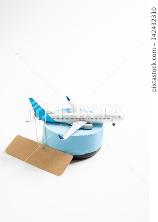 Model airplane on a blue stand with a blank brown luggage tag against a white background, representing travel, tourism, and flight bookings. Mockup or Copyspace 142432310