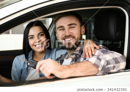 Happy couple with car key sitting in modern auto at dealership Happy couple with car key sitting in modern auto at dealership 142432391