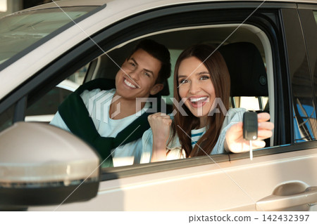 Happy couple with car key sitting in modern auto at dealership 142432397