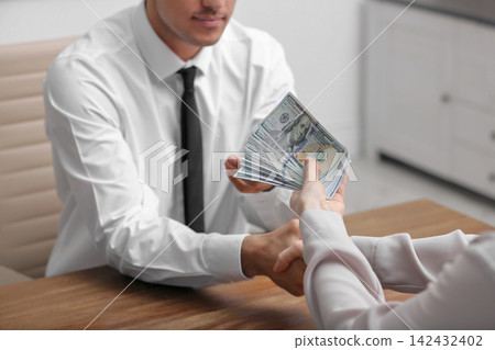 Woman shaking hands with man and offering bribe at table indoors, closeup Woman shaking hands with man and offering bribe at table indoors, closeup 142432402