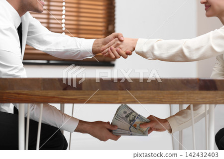 Woman shaking hands with man and giving bribe under table in office, closeup Woman shaking hands with man and giving bribe under table in office, closeup 142432403