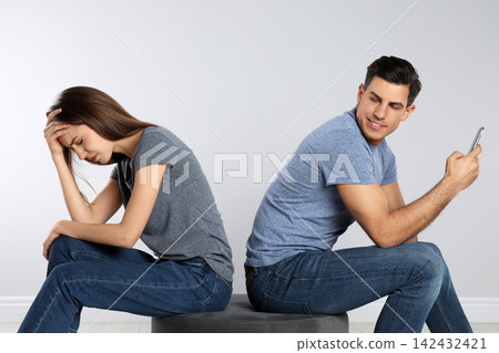 Man with smartphone mocking his girlfriend on grey background. Relationship problems Man with smartphone mocking his girlfriend on grey background. Relationship problems 142432421