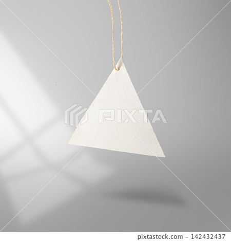 Blank triangular white paper price tag hanging from a rustic twine string against a grey background with soft shadow overlay. Mockup or Copyspace Blank triangular white paper price tag hanging from a rustic twine string against a grey background with soft shadow overlay. Mockup or Copyspace 142432437