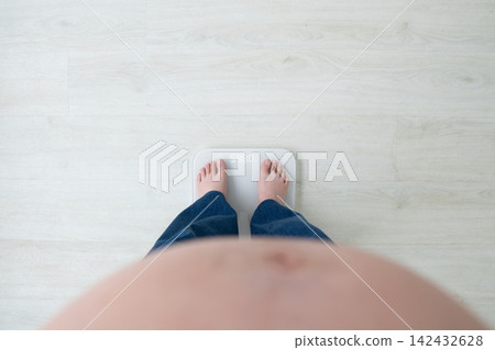 Pregnant woman with big belly standing on weight scale at home. Healthy weight gain during pregnancy avoid pregnancy complications such as gestational diabetes, preeclampsia, and cesarean delivery. 142432628