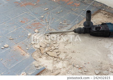 A powerful hammer drill with an orange glove rests on a concrete floor covered in debris A powerful hammer drill with an orange glove rests on a concrete floor covered in debris 142432815