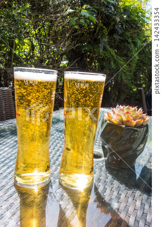 A frothy beer in a tall, slender glass sits on a table in the bright sunlight at a pub in the suburbs of London. A frothy beer in a tall, slender glass sits on a table in the bright sunlight at a pub in the suburbs of London. 142433354