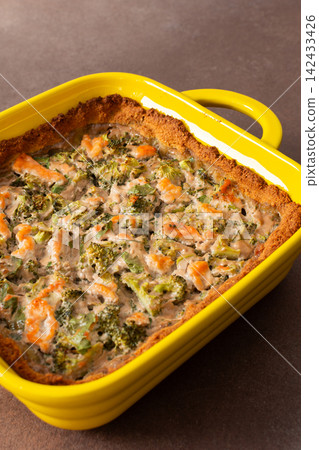 A gluten-free pie is placed in a bright yellow baking dish. It contains pieces of red fish and broccoli mixed with other ingredients. This dish is suitable for breakfast or lunch A gluten-free pie is placed in a bright yellow baking dish. It contains pieces of red fish and broccoli mixed with other ingredients. This dish is suitable for breakfast or lunch 142433426