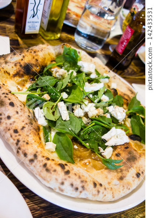 Authentic Italian cuisine: Pizza topped with tomatoes, cheese, and arugula, and a salad, at a restaurant in the suburbs of London. Authentic Italian cuisine: Pizza topped with tomatoes, cheese, and arugula, and a salad, at a restaurant in the suburbs of London. 142433531