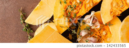 Yellow squash sliced into pieces is placed on a brown surface. Garlic cloves and fresh thyme are nearby, adding texture and color to the arrangement of vegetables, banner Yellow squash sliced into pieces is placed on a brown surface. Garlic cloves and fresh thyme are nearby, adding texture and color to the arrangement of vegetables, banner 142433565