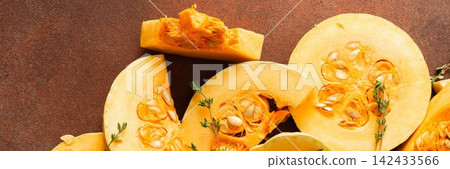 Pumpkin slices are arranged on a kitchen counter with fresh herbs nearby. The scene shows the preparation of seasonal dishes in the fall, banner Pumpkin slices are arranged on a kitchen counter with fresh herbs nearby. The scene shows the preparation of seasonal dishes in the fall, banner 142433566