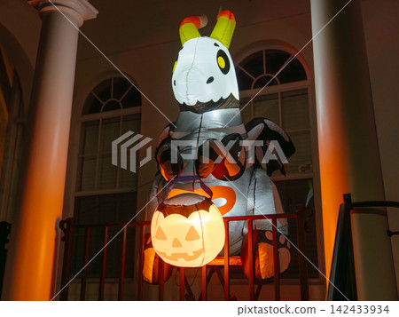 A large skeleton zebra inflatable holds a bright jack-o-lantern on a residential porch. Warm orange lighting creates a festive and spooky Halloween display at night. A large skeleton zebra inflatable holds a bright jack-o-lantern on a residential porch. Warm orange lighting creates a festive and spooky Halloween display at night. 142433934