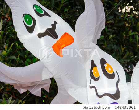 A close view of glowing inflatable ghosts highlights cheerful Halloween decorations. The illuminated display adds festive charm to an outdoor holiday setting. A close view of glowing inflatable ghosts highlights cheerful Halloween decorations. The illuminated display adds festive charm to an outdoor holiday setting. 142433961