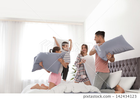 Happy family having pillow fight in bedroom Happy family having pillow fight in bedroom 142434123