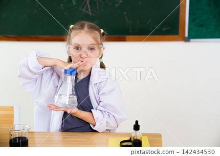 Little girl in lab coat holding a flask in a science classroom Little girl in lab coat holding a flask in a science classroom 142434530
