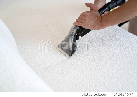 Professional cleaning of a white fabric sofa using a steam vacuum extractor nozzle. Professional cleaning of a white fabric sofa using a steam vacuum extractor nozzle. 142434574