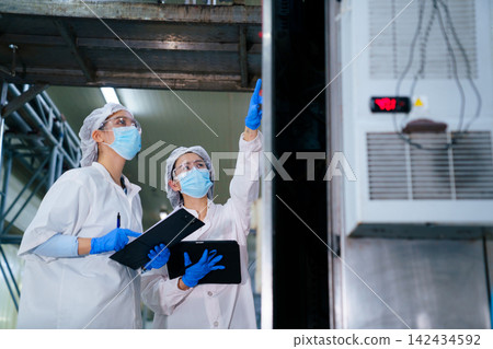 Female quality control inspectors wearing masks and goggles discussing production data 142434592