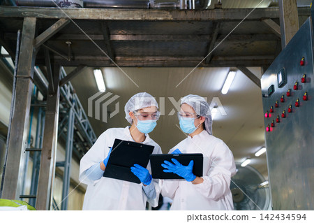 Female quality control inspectors wearing masks and goggles discussing production data Female quality control inspectors wearing masks and goggles discussing production data 142434594
