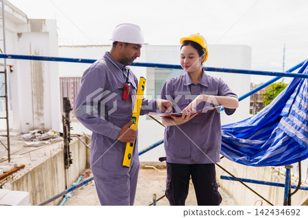 Male and female builders with hard hats and spirit level checking blueprints Male and female builders with hard hats and spirit level checking blueprints 142434692