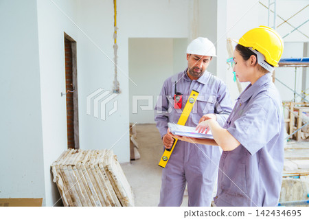 Male and female builders with hard hats and spirit level checking blueprints Male and female builders with hard hats and spirit level checking blueprints 142434695