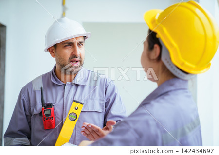 Male and female builders with hard hats and spirit level checking blueprints Male and female builders with hard hats and spirit level checking blueprints 142434697