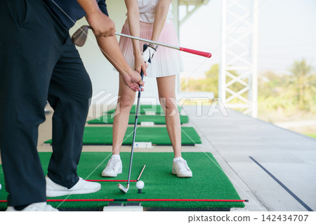 Young Asian woman practicing golf swing with instructor at a driving range Young Asian woman practicing golf swing with instructor at a driving range 142434707