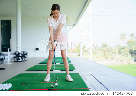 Close-up of female golfer addressing the ball at driving range Close-up of female golfer addressing the ball at driving range 142434708