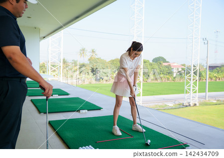 Close-up of female golfer addressing the ball at driving range Close-up of female golfer addressing the ball at driving range 142434709