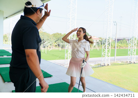 Happy Asian woman golfer giving high-five to instructor at driving range Happy Asian woman golfer giving high-five to instructor at driving range 142434711