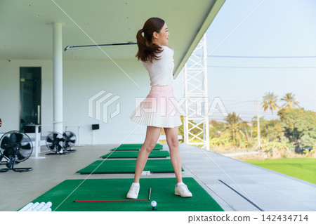 Active Asian woman enjoying golf practice session at driving range Active Asian woman enjoying golf practice session at driving range 142434714