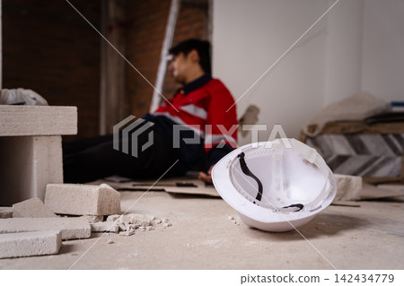 White hard hat on floor with injured construction worker in background White hard hat on floor with injured construction worker in background 142434779