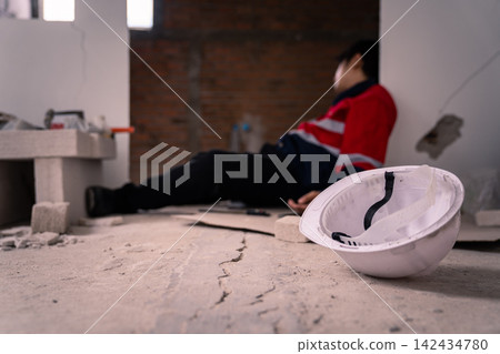 White hard hat on floor with injured construction worker in background White hard hat on floor with injured construction worker in background 142434780