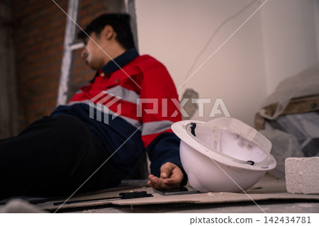 White hard hat on floor with injured construction worker in background 142434781