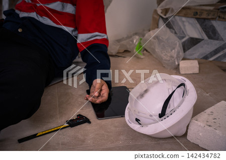 White hard hat on floor with injured construction worker in background 142434782