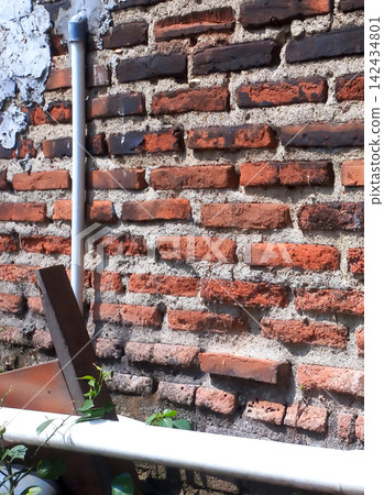 Weathered red and black brick walls with cement mortar and white pipes. 142434801