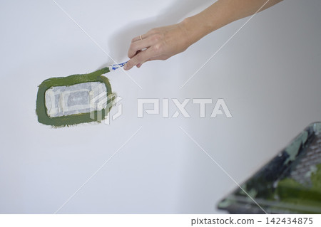 Hand applies green paint around masked electrical outlet with small brush Hand applies green paint around masked electrical outlet with small brush 142434875