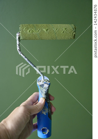 Hand holding paint roller covered with green paint in front of freshly painted wall Hand holding paint roller covered with green paint in front of freshly painted wall 142434876
