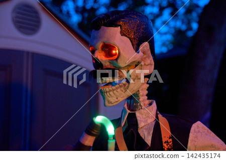 Side view of a skeleton bartender pouring a drink with a neon tube. Red glowing eyes and formal clothes create a spooky Halloween yard prop. Side view of a skeleton bartender pouring a drink with a neon tube. Red glowing eyes and formal clothes create a spooky Halloween yard prop. 142435174