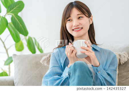 A woman relaxing on her sofa at home, drinking coffee and hot drinks. A woman relaxing on her sofa at home, drinking coffee and hot drinks. 142435327