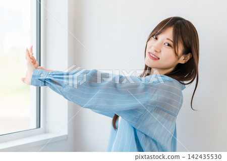 A young woman comfortably stretching by the window in the morning. 142435530