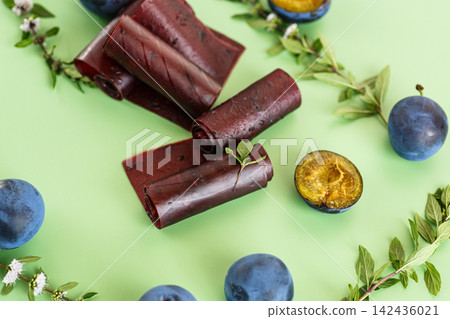 Healthy plum fruit leather with fresh fruit on light green background Healthy plum fruit leather with fresh fruit on light green background 142436021