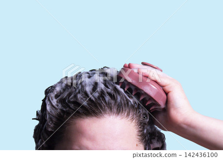 Pink scalp massager brush for hair treatment and care in human hand on blue background Pink scalp massager brush for hair treatment and care in human hand on blue background 142436100