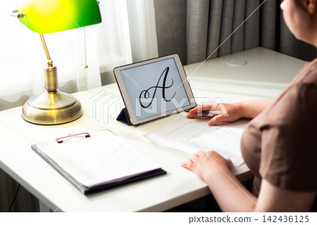 Person seated at desk deeply focused on writing in notebook. Physical engagement of motor skills Handwriting as brain training. Prevention of age related cognitive decline. Senior or adult practicing 142436125