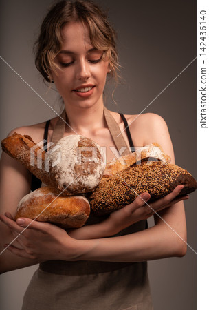Young woman baker holding fresh artisanal bread loaves, presenting organic bakery products Young woman baker holding fresh artisanal bread loaves, presenting organic bakery products 142436140