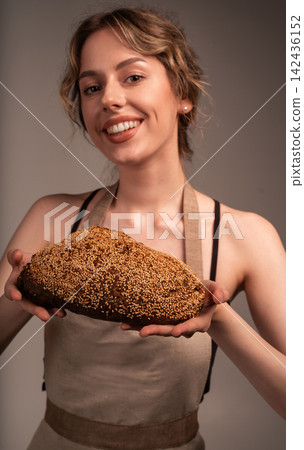 Smiling woman baker holding fresh homemade artisan bread with sesame seeds, representing freshness and healthy food Smiling woman baker holding fresh homemade artisan bread with sesame seeds, representing freshness and healthy food 142436152
