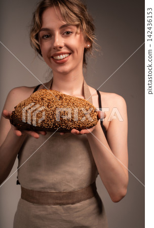 Smiling woman baker presenting fresh baked artisan sesame bread loaf, holding dark rustic sourdough with hands Smiling woman baker presenting fresh baked artisan sesame bread loaf, holding dark rustic sourdough with hands 142436153