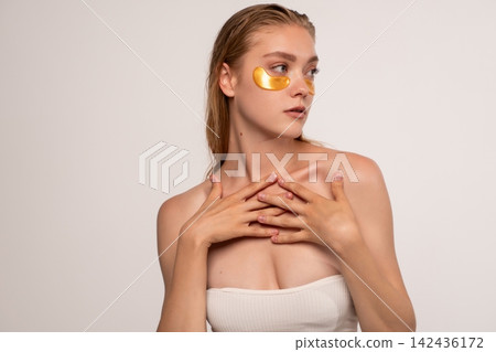 Young woman wearing gold eye patches for under eye skin care, enjoying wellness and facial beauty treatment Young woman wearing gold eye patches for under eye skin care, enjoying wellness and facial beauty treatment 142436172