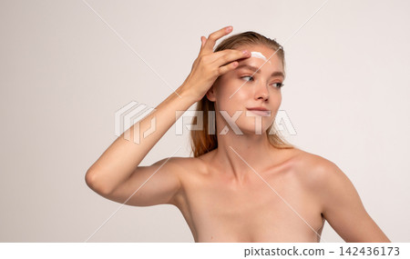 Woman applying facial cream on forehead against a white background, focusing on daily beauty and glow Woman applying facial cream on forehead against a white background, focusing on daily beauty and glow 142436173