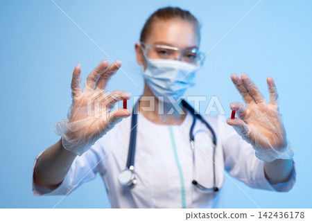 Medical professional wearing protective gear holding red capsules in gloved hands during healthcare examination Medical professional wearing protective gear holding red capsules in gloved hands during healthcare examination 142436178