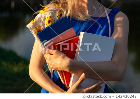 Woman holding stack of books in hands in green park. Book lover day celebration. Self education and digital detox concept 142436242